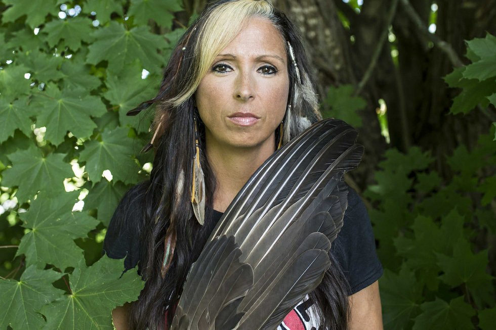 Pam Palmater holding a feature and standing in front of a tree.